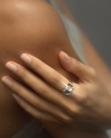 Close-up of a person hand wearing a silver diamond ring resting gently against a bare shoulder