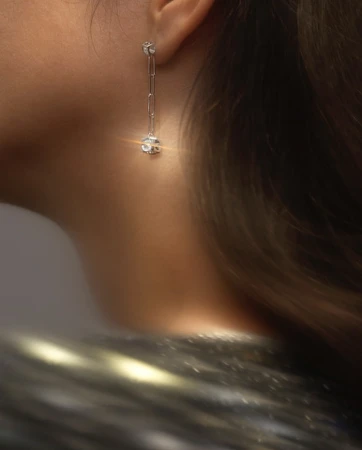 Elegant long silver chain earrings worn by a woman, close-up capturing ear and neck details with blurred textured clothing.