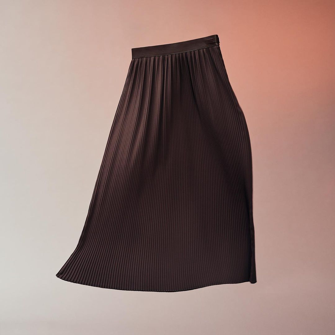 Dark brown pleated midi skirt in a studio shot with a light peach and orange gradient background. Fashionable and elegant clothing item.
