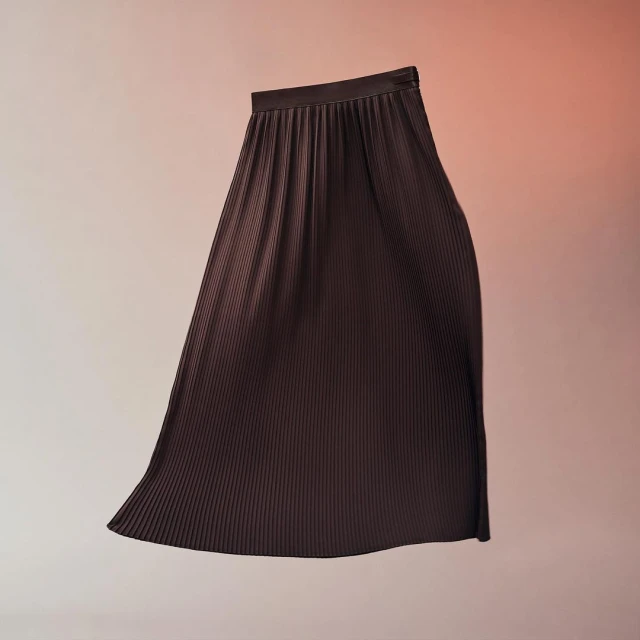 Dark brown pleated midi skirt in a studio shot with a light peach and orange gradient background. Fashionable and elegant clothing item.