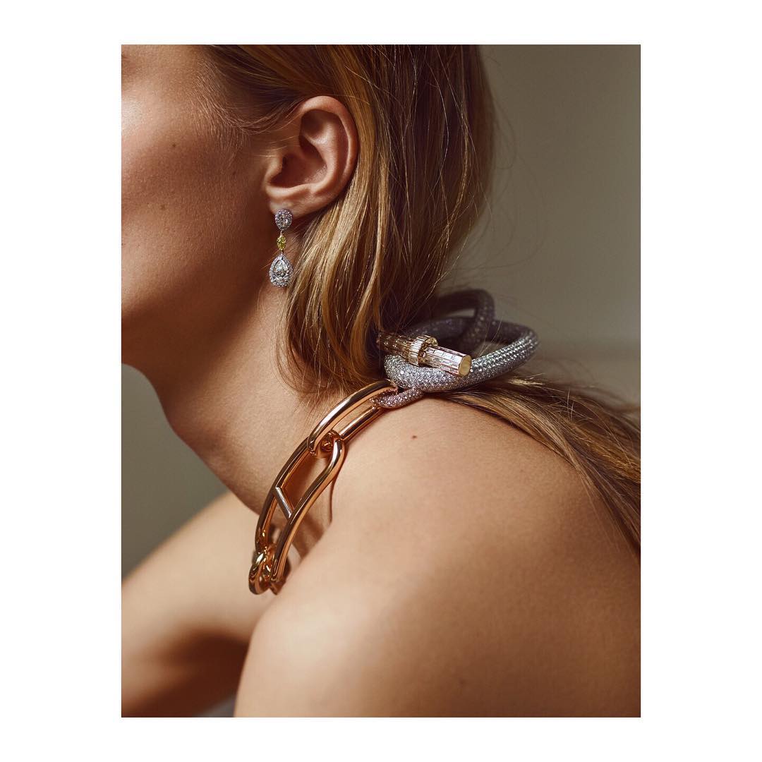 Close-up shot of an adult female model wearing a large gold chain necklace and jeweled earrings, and bracelets in an indoor setting.