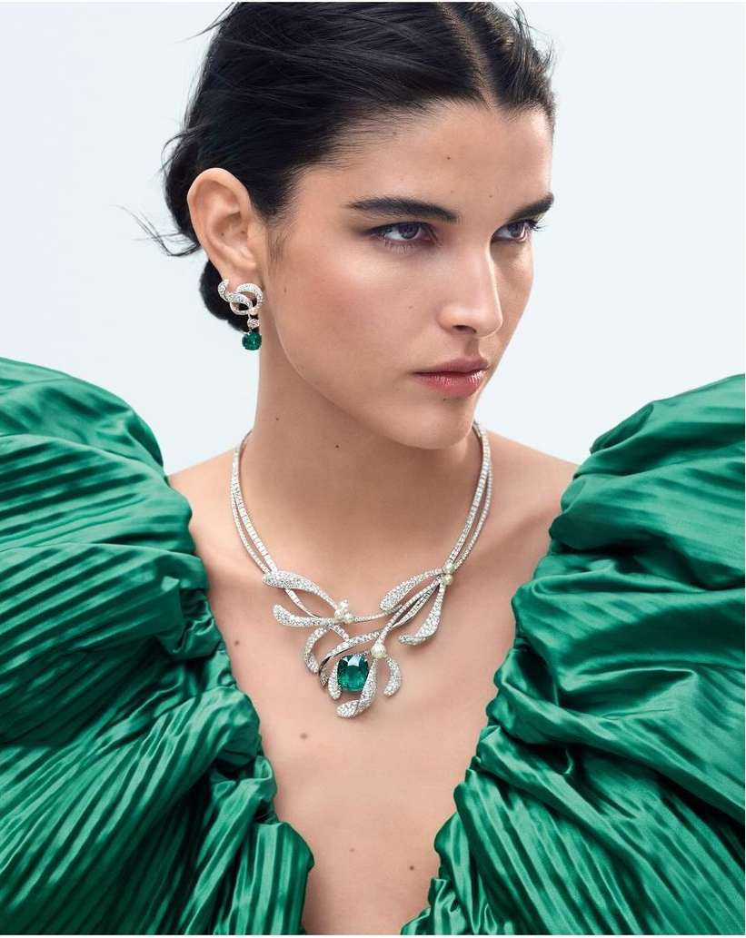 Woman wearing emerald and diamond jewelry and a green dress in a studio shot for a beauty and fashion editorial.