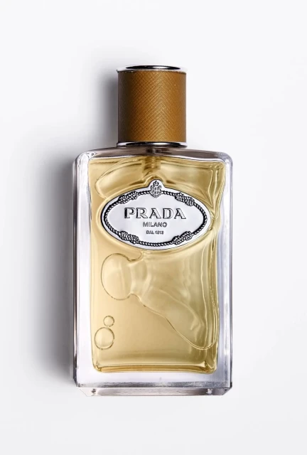 Close-up studio shot of a Prada fragrance bottle with a tan cap and clear glass, set against a bright white backdrop.