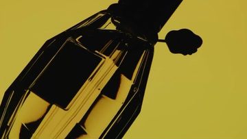 Close-up studio shot of a perfume bottle against a yellow backdrop, highlighting the geometric shape and dark shadow of the bottle.