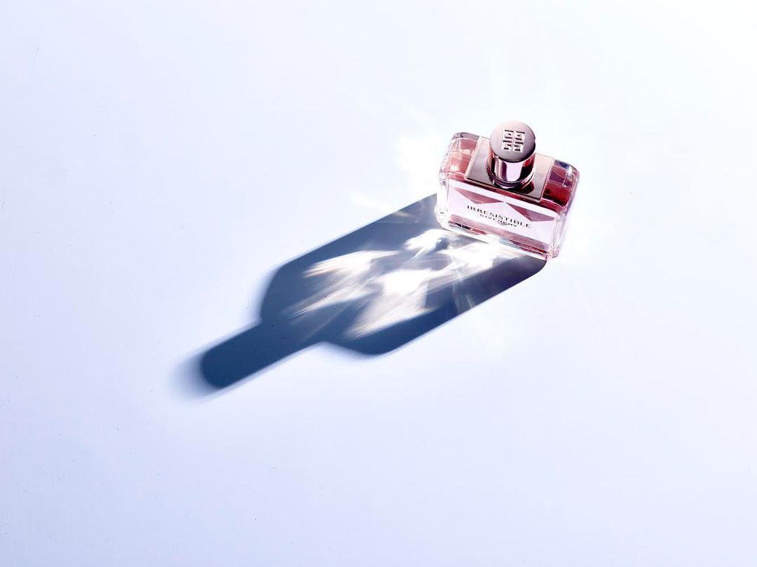 Studio shot of a pink Givenchy Irresistible fragrance bottle on a light blue surface casting a shadow, product photography.
