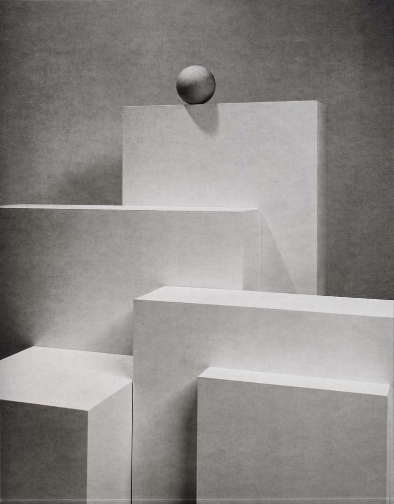 Abstract still life features white geometric platforms with shadows and a sphere on top, creating a minimalist composition on a gray background.