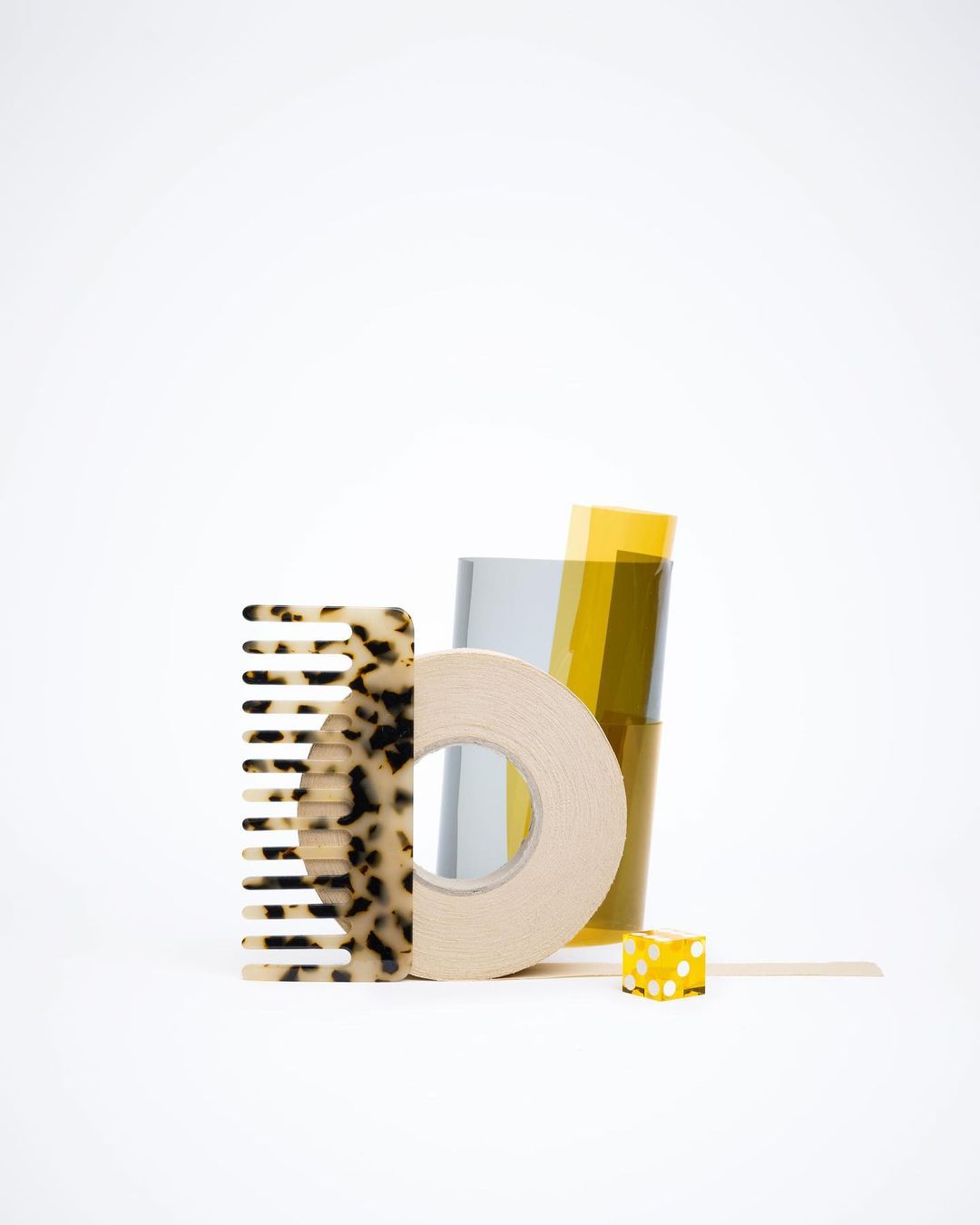 Still life of comb, tape, films, and a cube on a white background, creating an artistic and minimalist studio product shot.