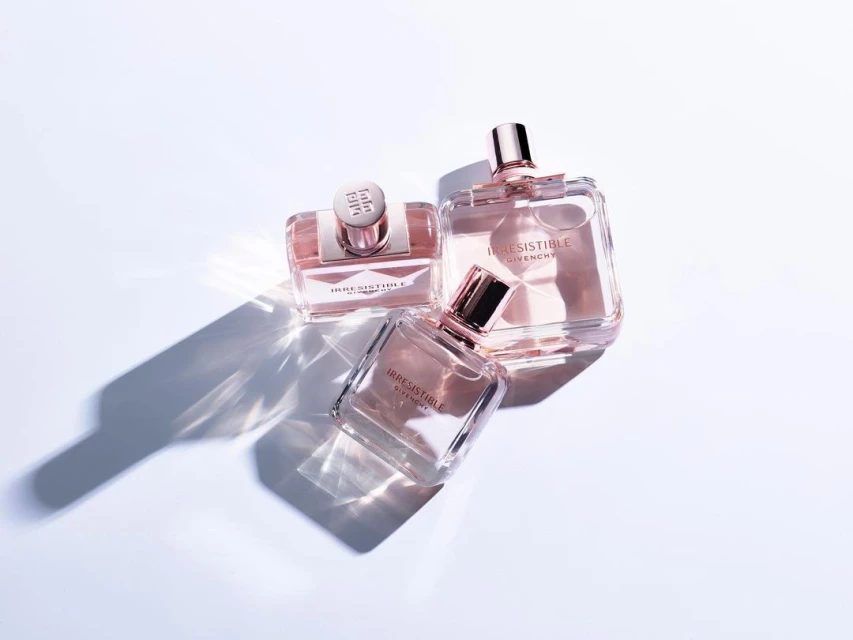 Three Givenchy Irresistible perfume bottles with rose gold accents are grouped on a white surface with light and shadow patterns.