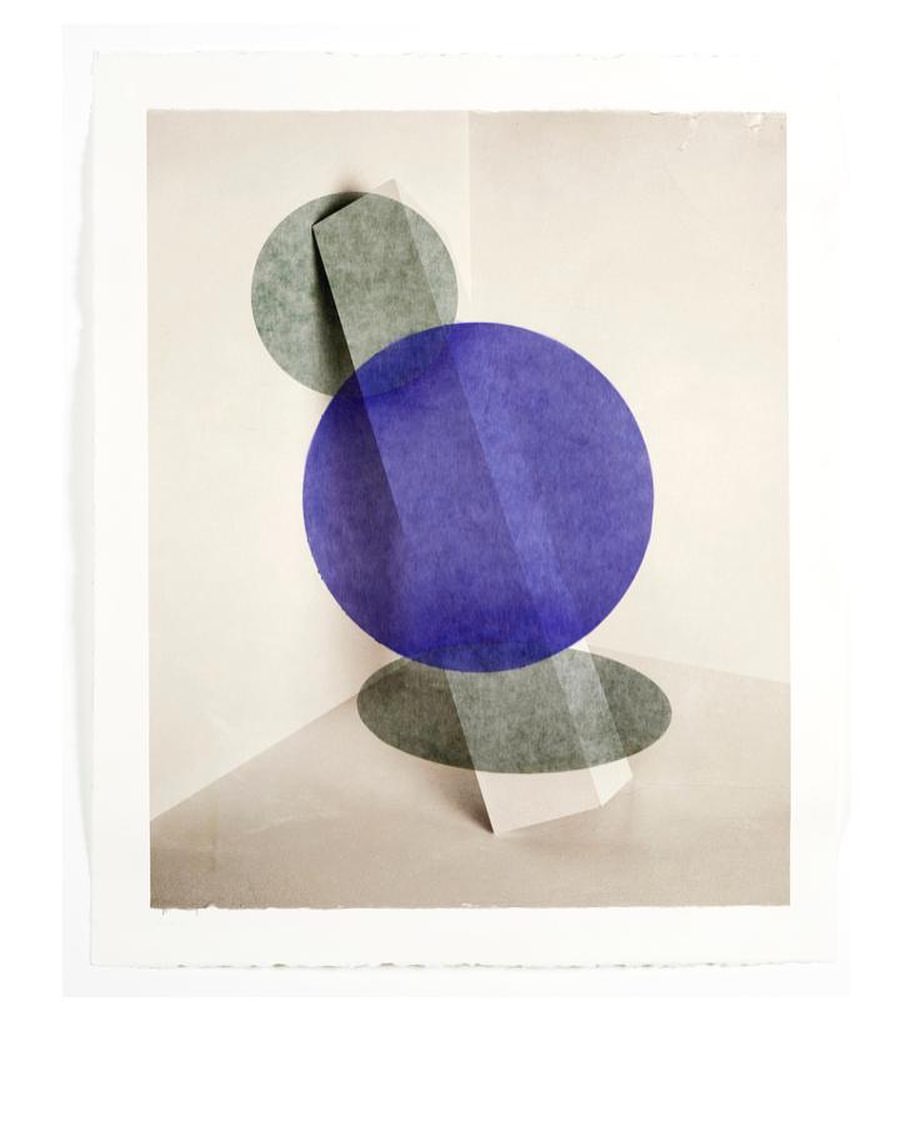 Abstract artwork featuring layered geometric shapes in blue and grey on a neutral backdrop. Artful presentation with torn edges and textured appearance.