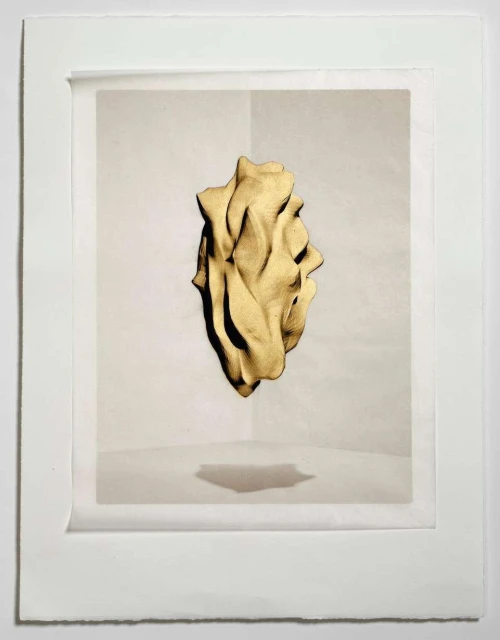 Abstract beige form on white corner wall, presented as framed photograph in white frame, casting shadow below.