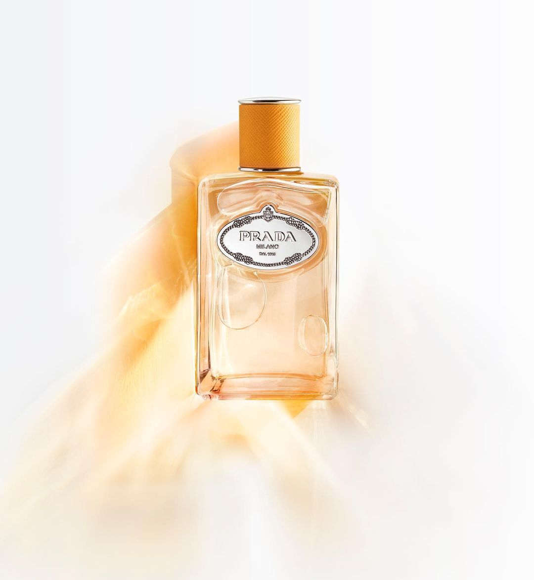 Prada perfume bottle on a white surface with orange smoke, showcasing a clean design and warm color palette in a studio setting.