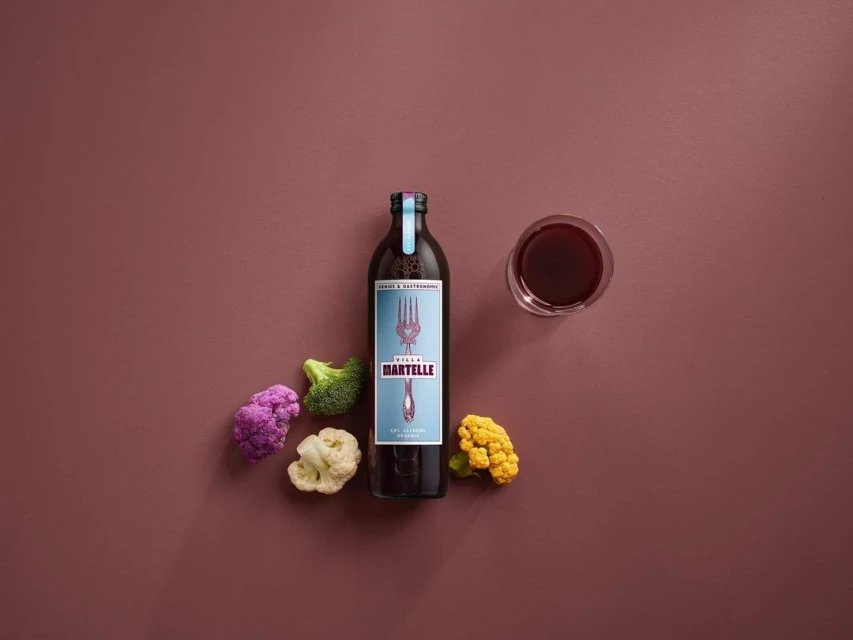 A bottle of Stella Martelle vegetable juice is displayed with cauliflower and a glass of juice on a maroon background.
