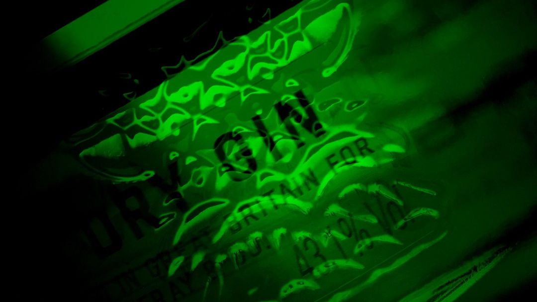 Close-up of a green-tinted Gin bottle, highlighting the brand name and label details, set against a dark background. 