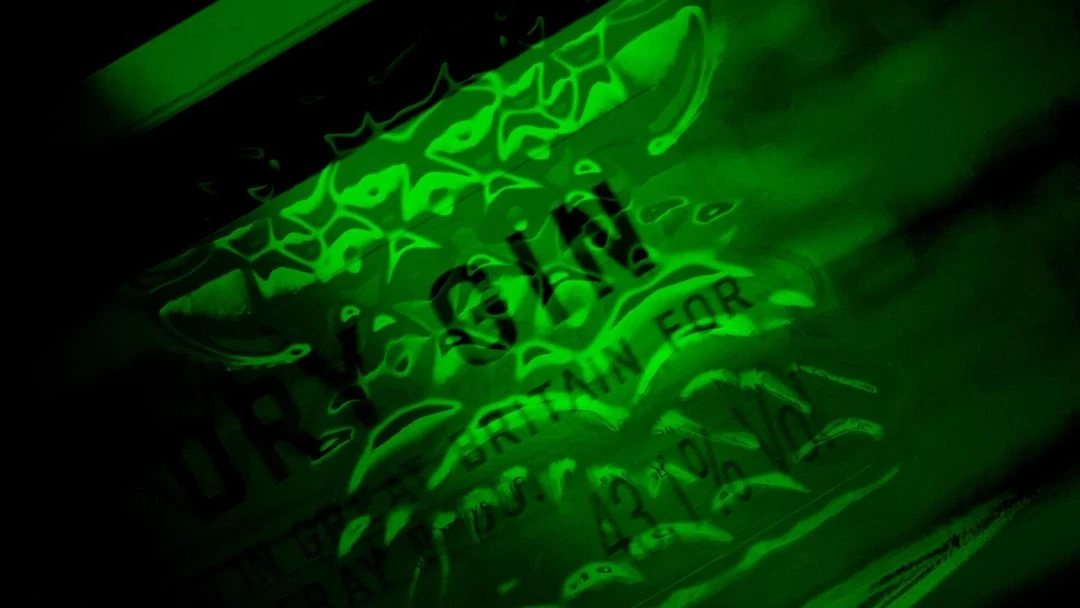 Close-up of a green-tinted Gin bottle, highlighting the brand name and label details, set against a dark background. 