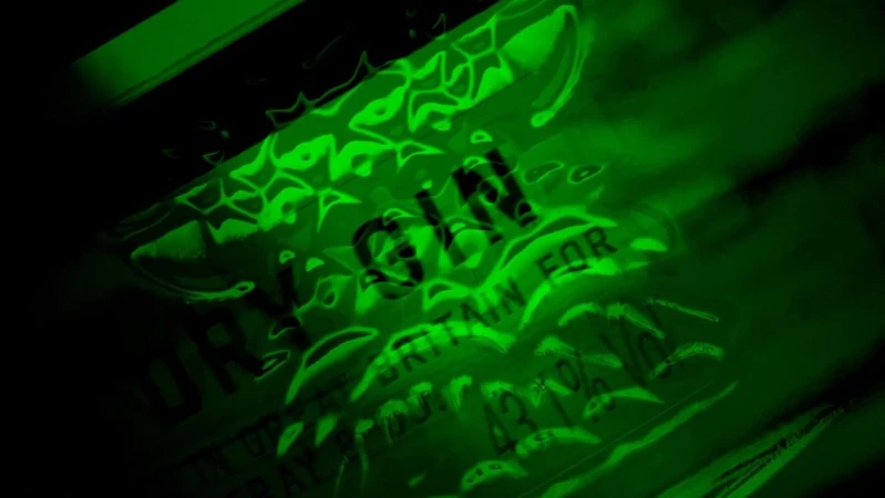 Close-up of a green-tinted Gin bottle, highlighting the brand name and label details, set against a dark background. 