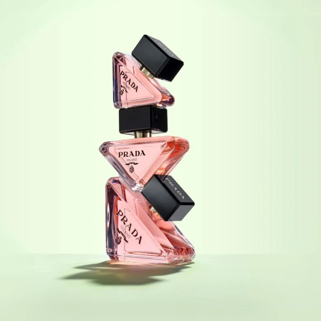 Stacked Prada Paradoxe perfume bottles with black caps and soft pink liquid on a light green gradient backdrop, modern beauty product shot.