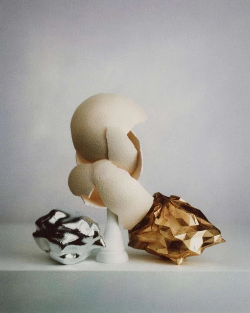 Still life photography featuring textured spheres, including a fragmented white sphere on a pedestal and crumpled metallic objects.