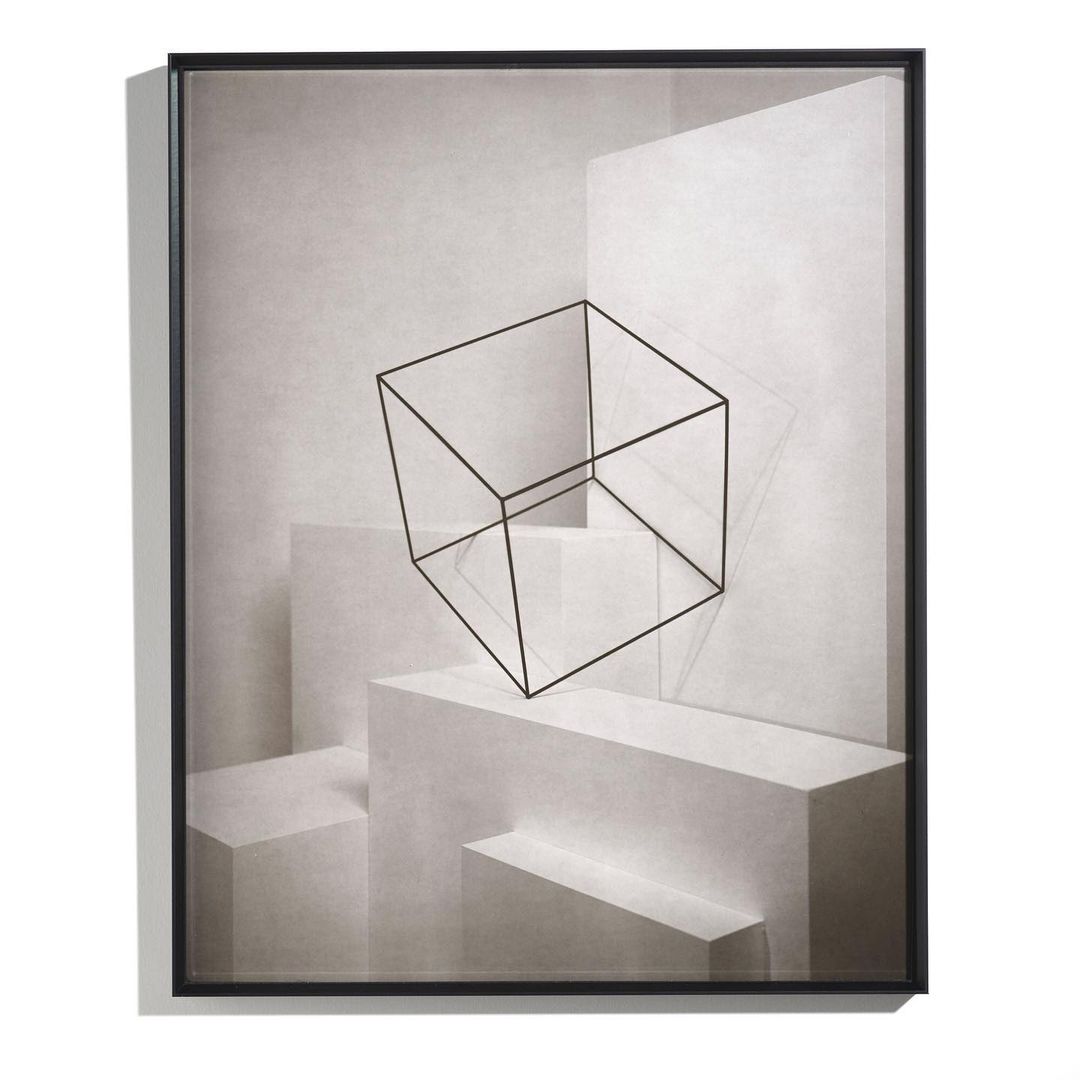Geometric art print with a black wireframe cube floating above white geometric shapes, all framed in black on a white background.