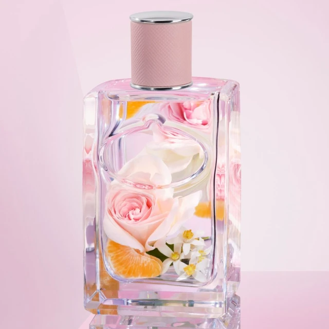 Crystal perfume bottle filled with rose and orange slices on a light pink surface, reflecting studio lighting, and beauty product. 