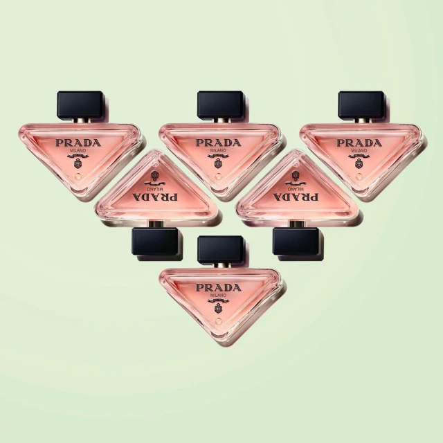 Arrangement of six Prada Paradoxe perfume bottles on a soft, light green background, showcasing their triangular shape and branding.