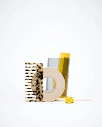 Still life arrangement of a tortoiseshell comb, a beige adhesive tape roll, and a yellow die on a white surface
