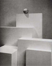 Monochrome still life composition featuring a small sphere balanced on top of geometric rectangular blocks against a textured grey background.