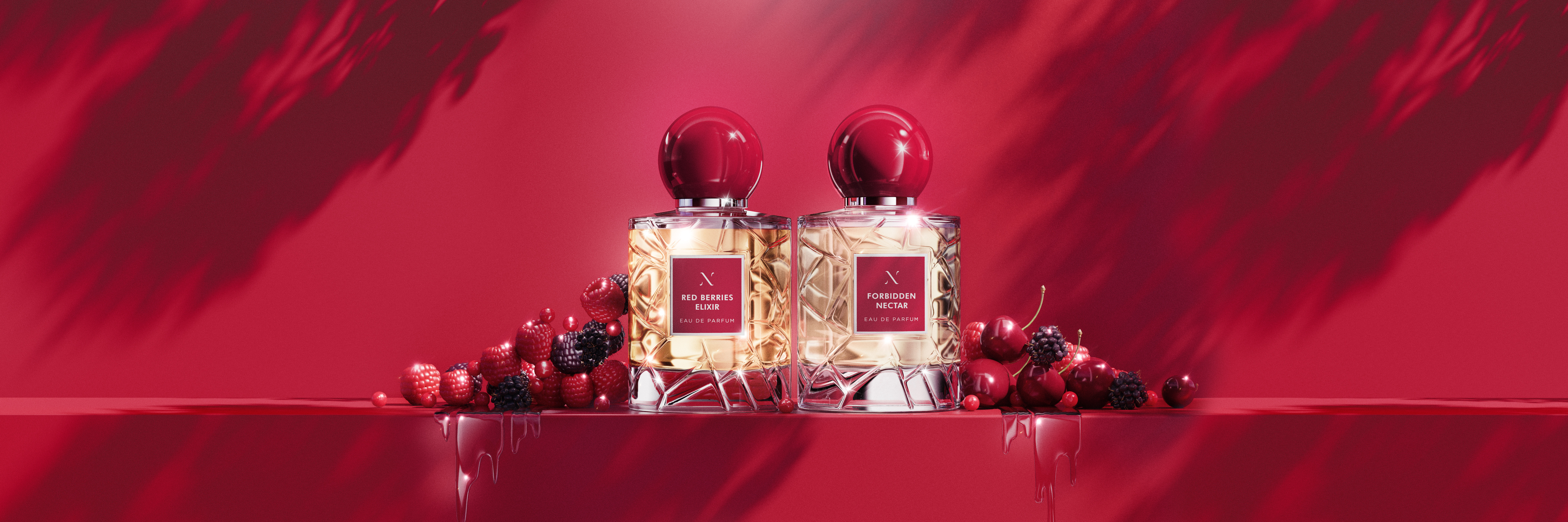 Two clear glass perfume bottles with red caps sit among red cherries, raspberries, and blackberries against a red backdrop.