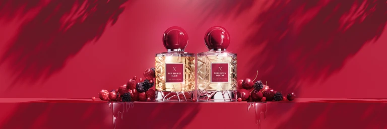 Two luxury perfume bottles with round red caps displayed on a red ledge with fresh berries and dappled leaf shadows.