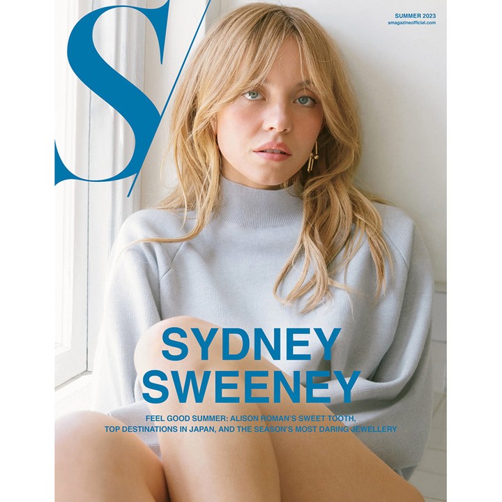 Magazine cover featuring Sydney Sweeney. She's wearing a blue top and sitting by a window with the magazine title in blue.