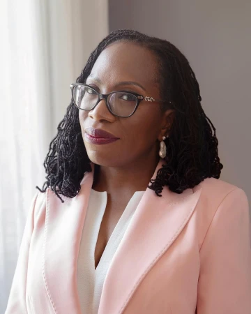 Portrait of a Black woman in her 40s wearing glasses, a pink blazer, and white top, photographed by Celeste Sloman.