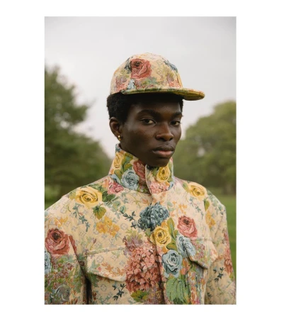 Portrait of a Black man wearing a floral patterned jacket and matching cap outdoors in a park.