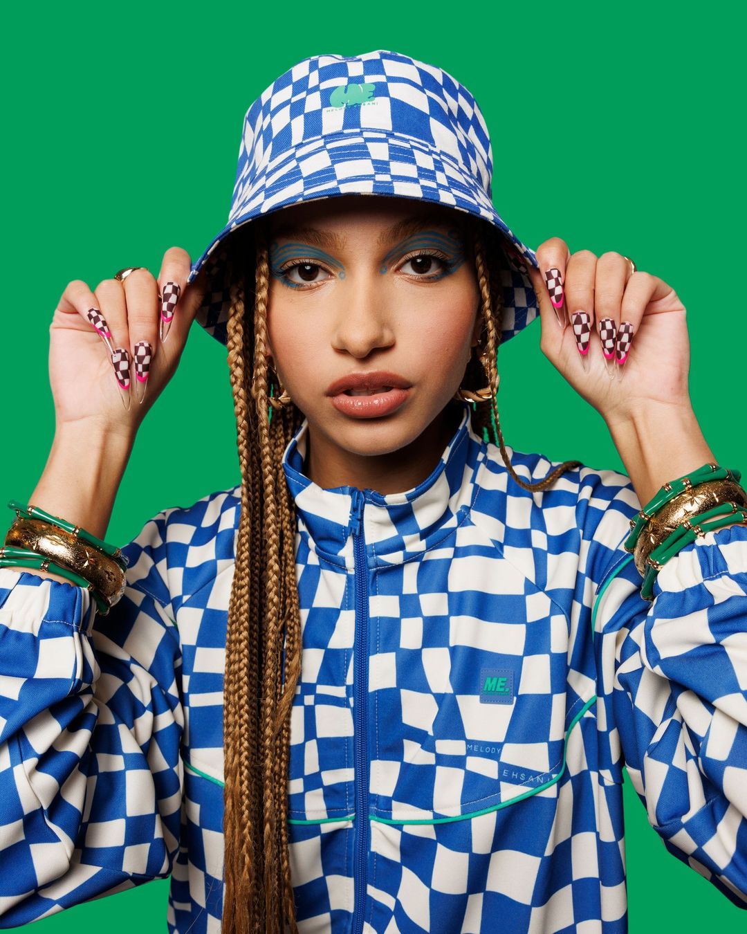 Woman in a checkered blue and white outfit with braids and green background, showcasing fashion and individual style in a studio setting.