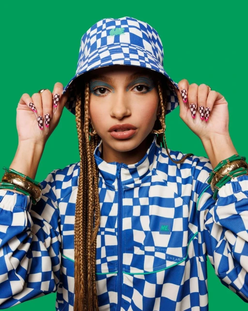 Woman in a checkered blue and white outfit with braids and green background, showcasing fashion and individual style in a studio setting.