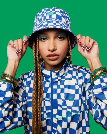 Woman in a checkered blue and white outfit with braids and green background, showcasing fashion and individual style in a studio setting.