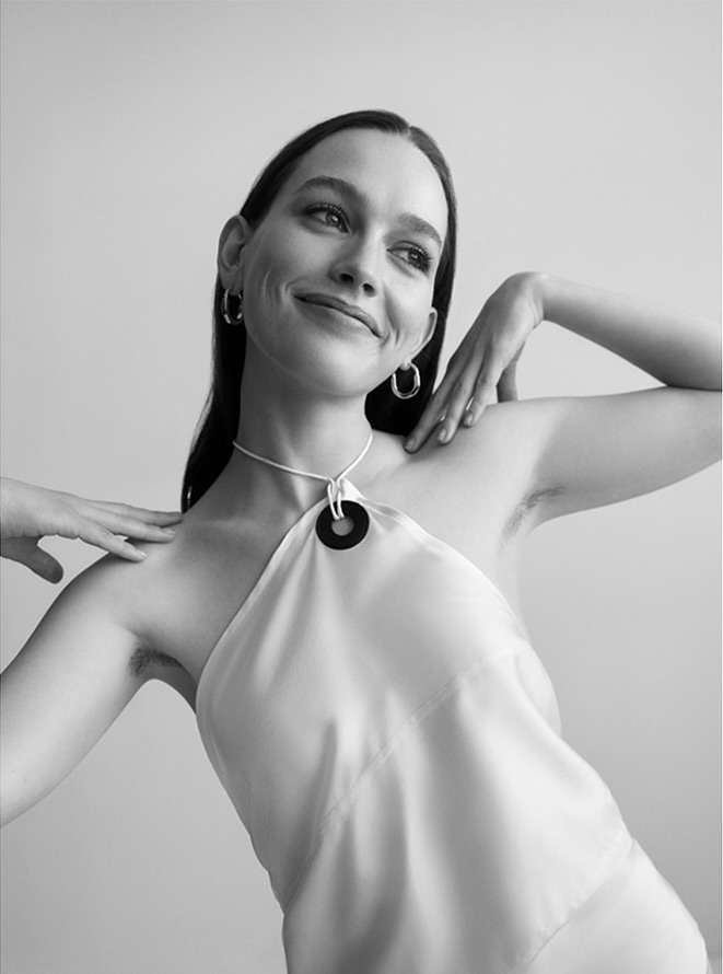 Monochrome portrait of a young woman with dark hair and hoop earrings posing in front of a white background wearing a halter top.