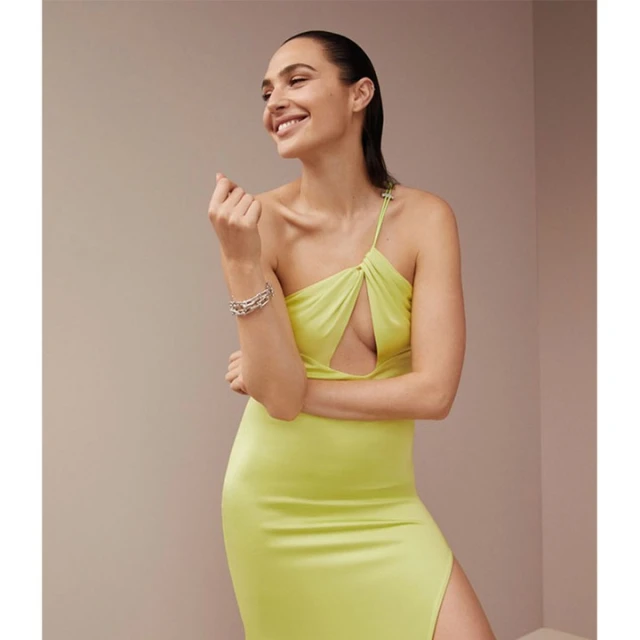 A woman with dark hair smiles while wearing a chartreuse dress, silver bracelet, and posing in a light, neutral-tone indoor setting.