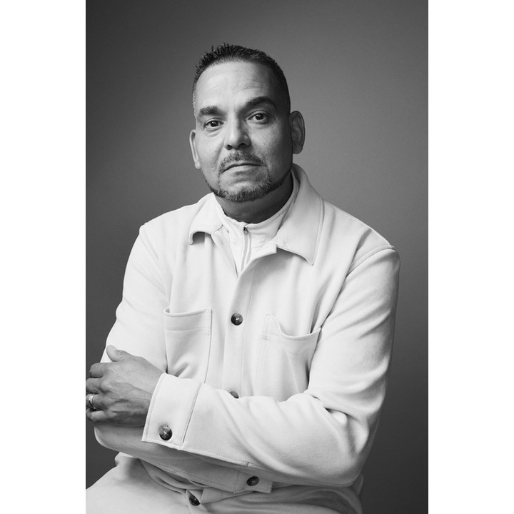 Portrait of a man in his 40s with short hair and goatee wearing a button-down jacket with arms crossed against a grey studio backdrop.