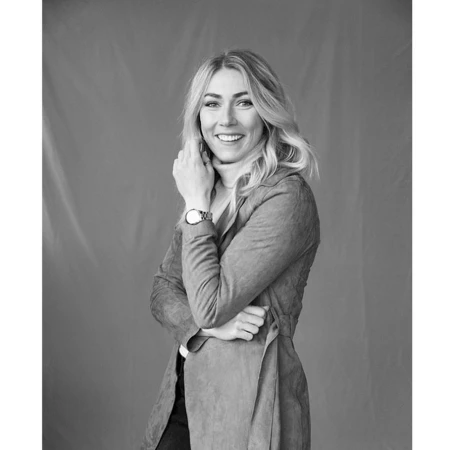 Portrait of a blonde woman wearing a belted coat and a wristwatch against a seamless backdrop
