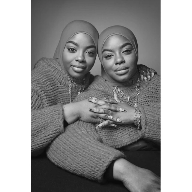 Black and white portrait of two women with headscarves and sweaters, adorned with jewelry, captured in a close-up studio shot.