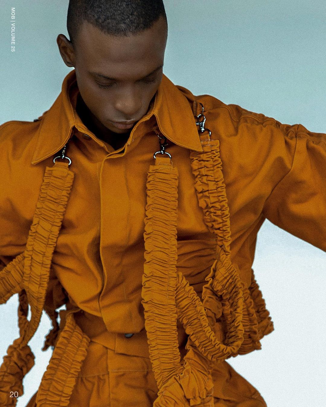 Fashion-forward portrait of a dark-skinned adult male in an orange button-down shirt and matching pants with ruched fabric straps.