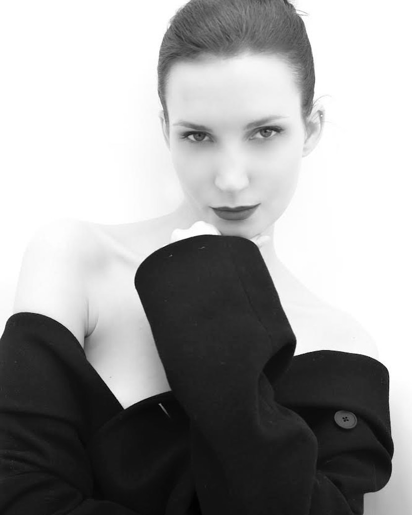 Black and white portrait of a woman with red lipstick wearing a black coat, posing against a white background in a photo studio.