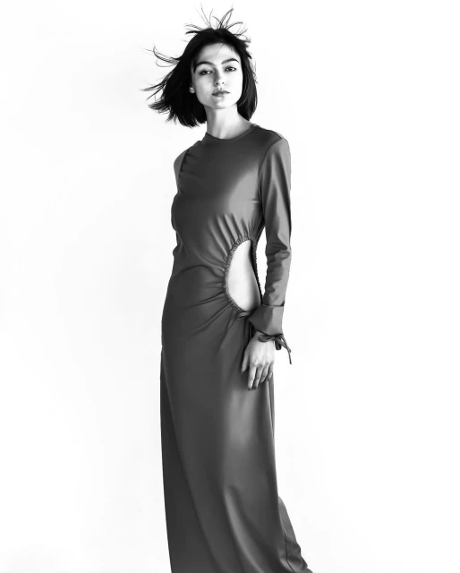 Black and white shot of a woman in a long dress with a cutout, posing in a studio with her hair blowing for a fashion editorial.