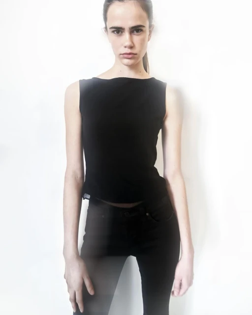 Studio shot of a slender woman wearing a black top and black jeans, standing against a white background with soft, diffused lighting.