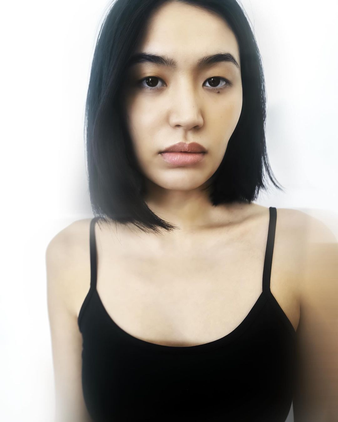 Portrait of a woman with short black hair wearing a black spaghetti strap top against a bright white background