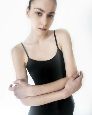 Model in a black slip dress with crossed arms against a plain white background captured by Celestia Seyvant in Milan.