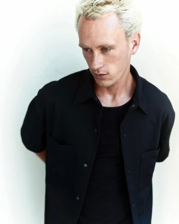 Portrait of a blonde man wearing a black button-down shirt against a plain white background
