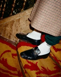 Close-up of feet wearing black leather loafers, white socks, green sweatpants, and a houndstooth skirt on stairs.