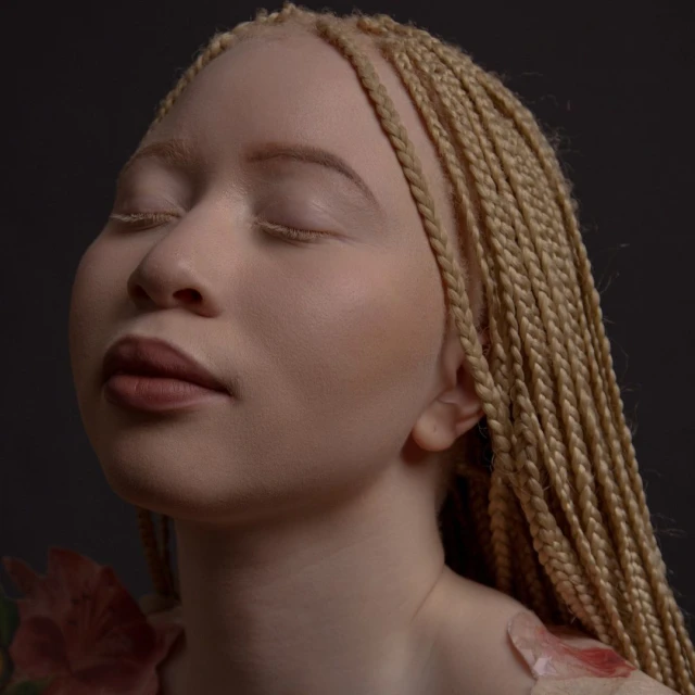 Close-up portrait of a woman with blonde braided hair and fair skin, eyes closed, with a dark grey background and red and green flowers.