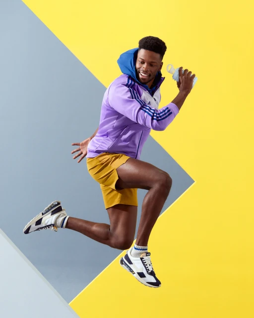 Athletic African-American man in sportswear jumping in front of a two-tone yellow and gray background while holding a water bottle.