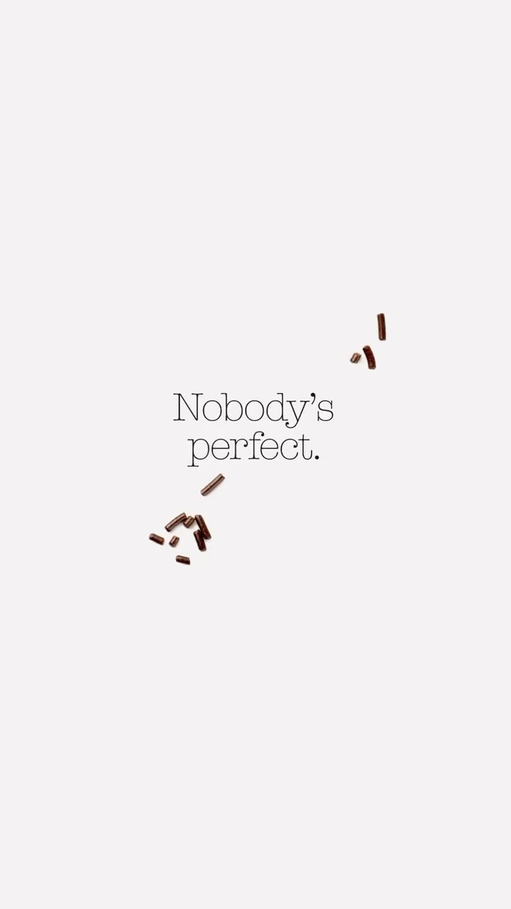 Scattered chocolate sprinkles on a white background with the text 'Nobody's perfect.' creates a minimalist, food-themed visual.
